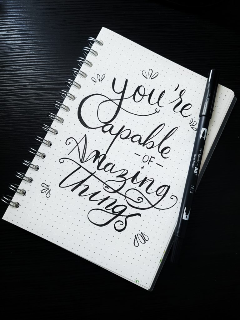 Notebook page with hand-lettered quote, “You’re capable of amazing things,” and a pen
