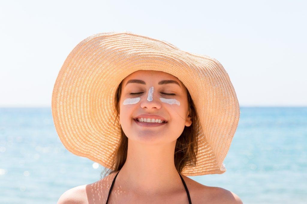 Smiling woman wearing a sun hat with sunscreen on her face at the beach