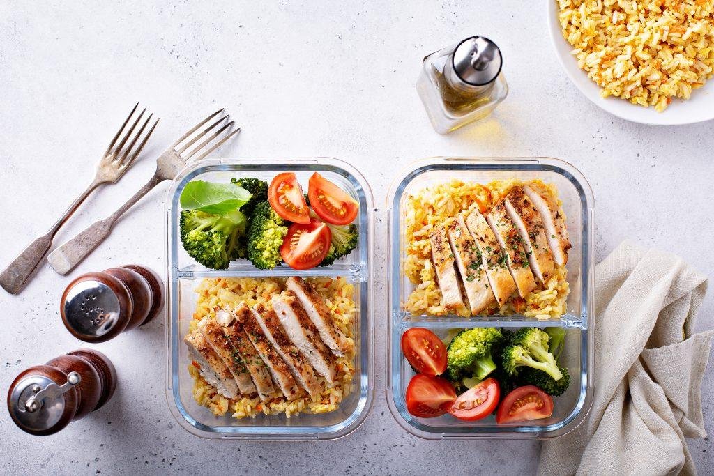 Meal prep containers with sliced chicken, rice, broccoli, and tomatoes