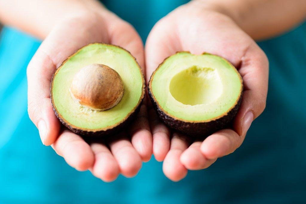 Two avocado halves held in cupped hands, one with the pit and one without