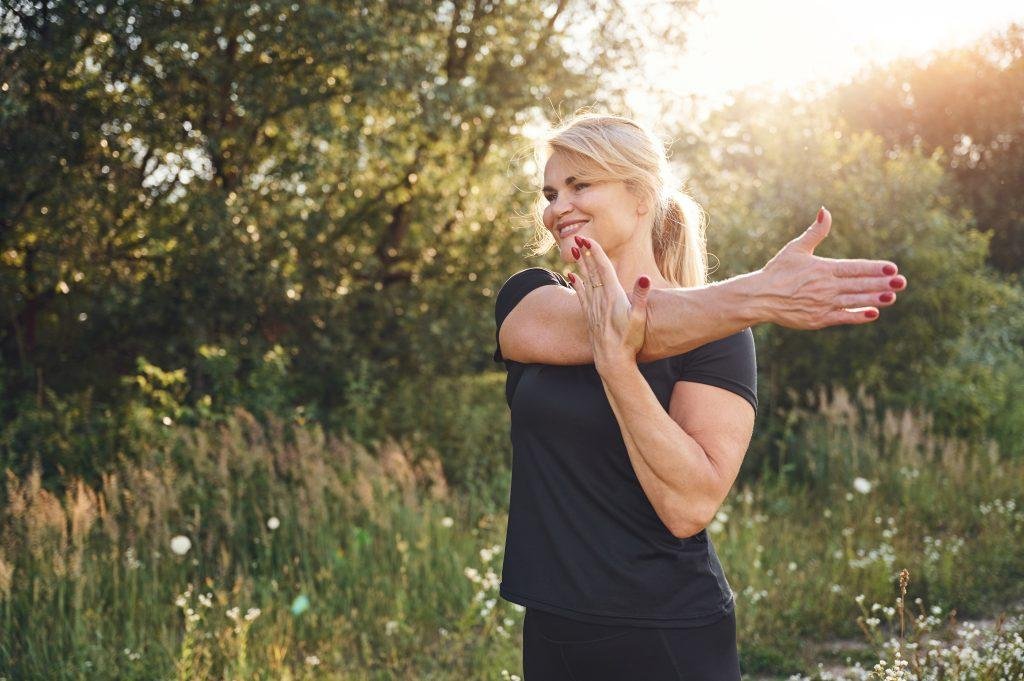 Woman stretching her arm outdoors in a sunlit park