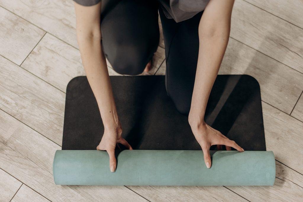 Person unrolling a yoga mat on a wooden floor