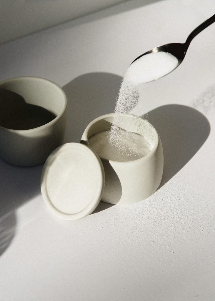 Spoon pouring sugar into a cup beside two other cups on a sunlit table