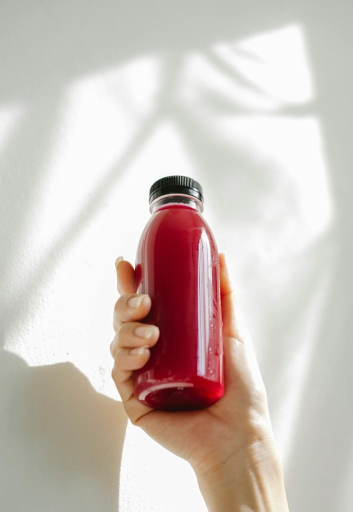Hand holding a red drink bottle with a black cap