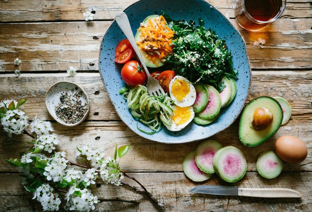 A salad bowl with avocado, eggs, tomatoes, greens, and sliced radishes on a rustic wooden table