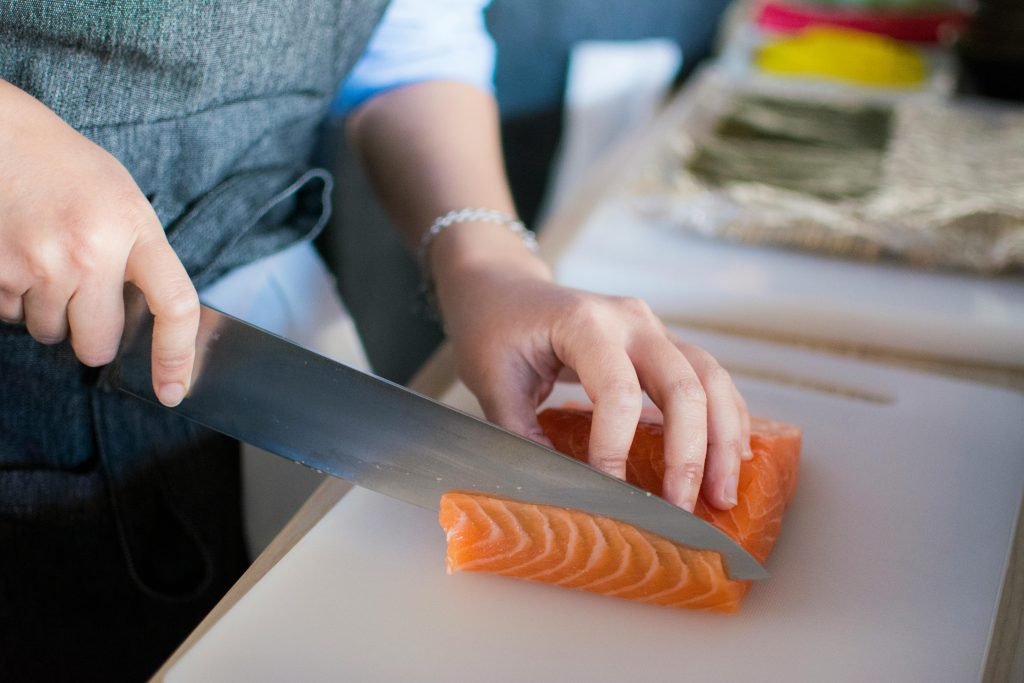 Person slicing a salmon fillet with a chef’s knife on a cutting board