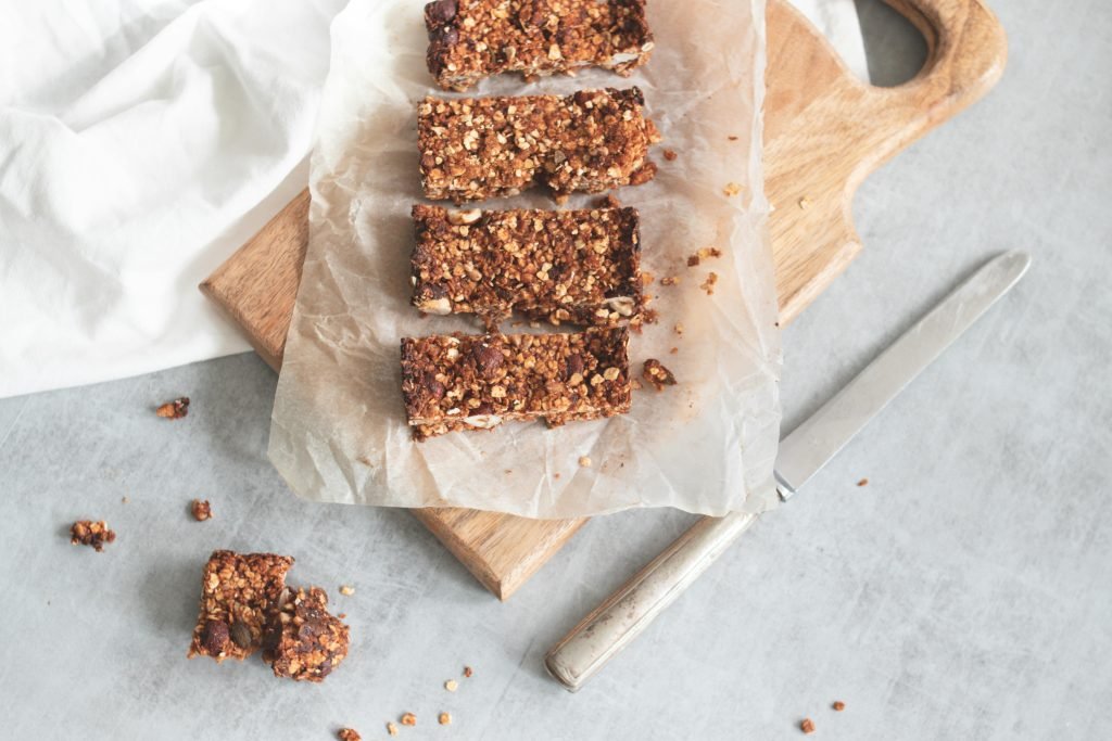 Granola bars on parchment paper on a wooden cutting board with a knife nearby