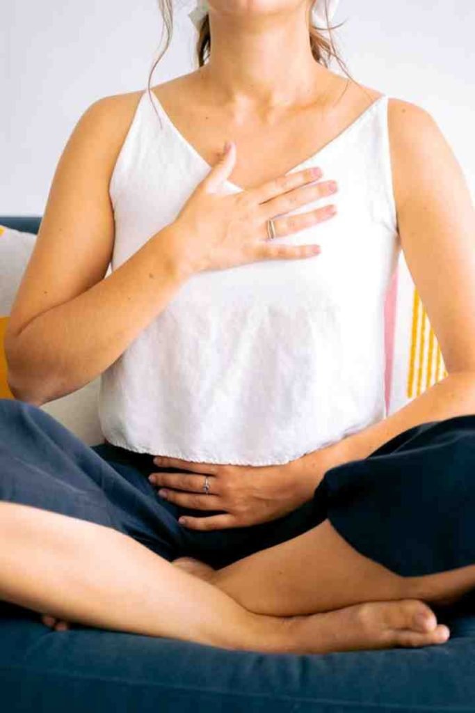Woman sitting cross-legged, placing one hand on her chest and one on her abdomen in a breathing exercise