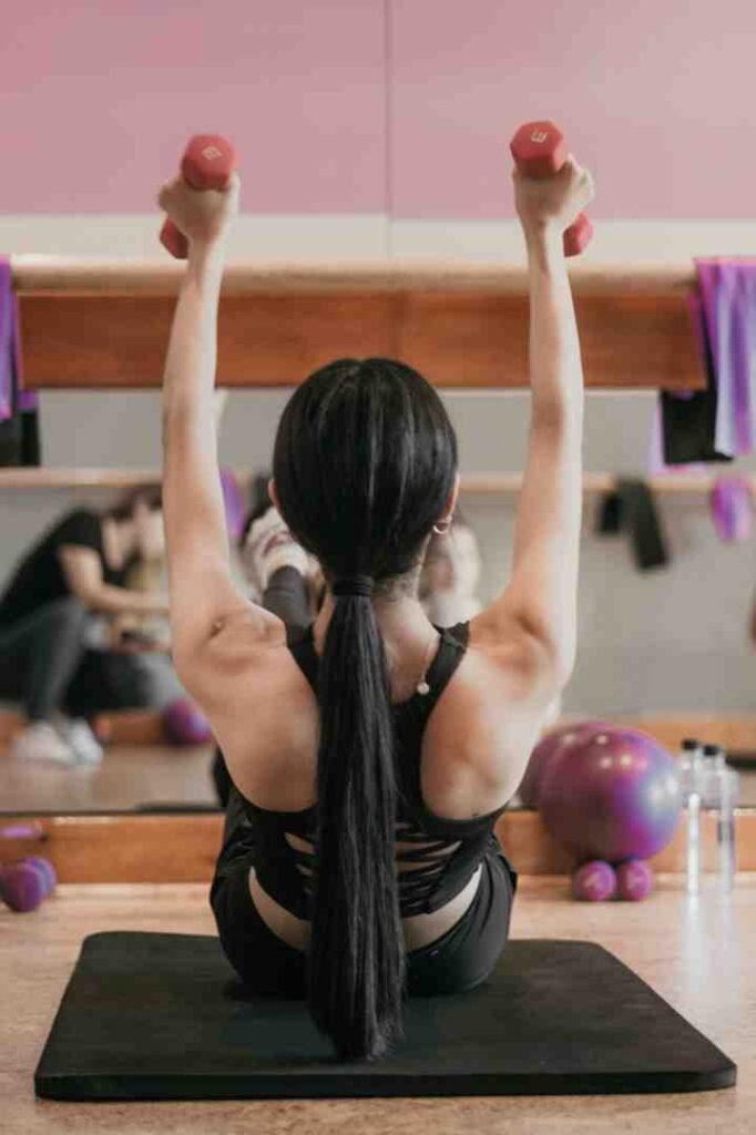 Woman doing seated dumbbell shoulder press in a gym studio